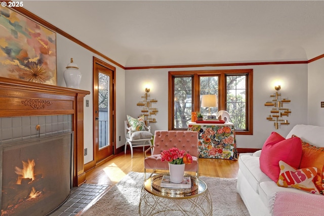 living room with a tiled fireplace, wood finished floors, baseboards, and ornamental molding