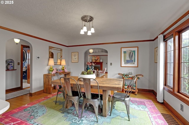 dining area featuring visible vents, ornamental molding, a textured ceiling, wood finished floors, and arched walkways