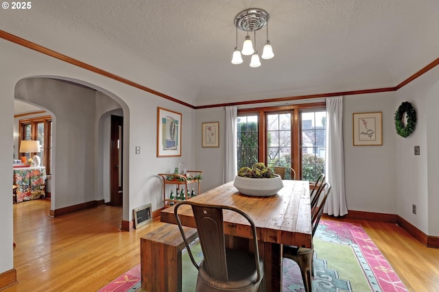 dining area featuring crown molding, baseboards, light wood-type flooring, arched walkways, and a textured ceiling