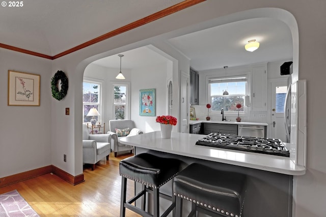 kitchen with a kitchen breakfast bar, gas cooktop, light wood-style floors, and arched walkways