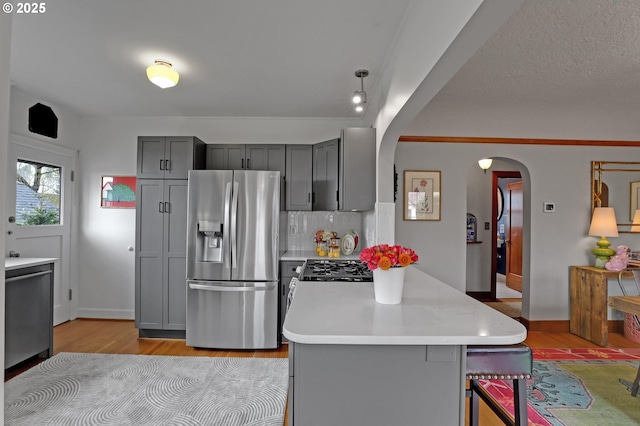 kitchen with light wood-style flooring, gray cabinets, arched walkways, stainless steel fridge with ice dispenser, and light countertops