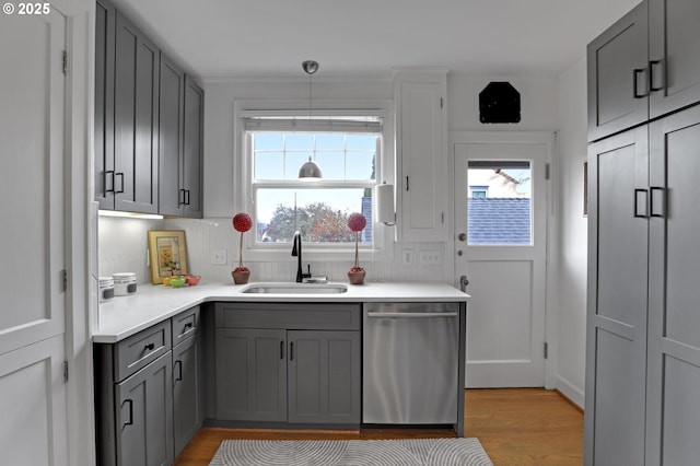 kitchen featuring gray cabinets, a sink, backsplash, light countertops, and dishwasher