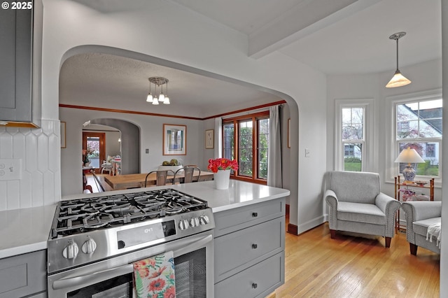 kitchen with arched walkways, light wood finished floors, gray cabinetry, and stainless steel gas range