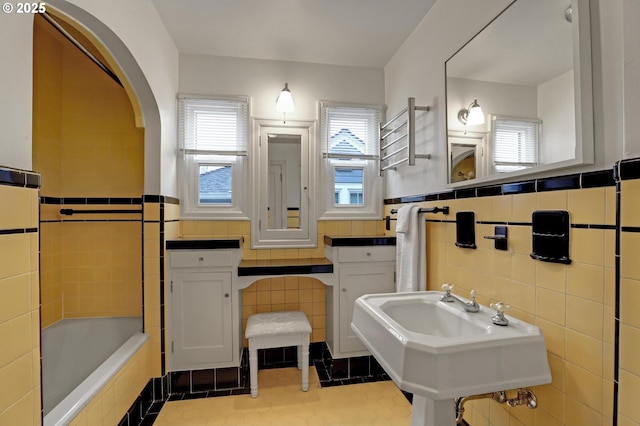 bathroom featuring tile patterned flooring, a tub, a wealth of natural light, and a sink