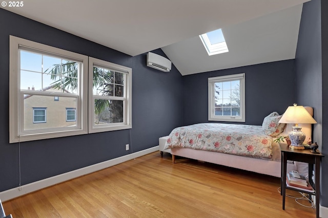 bedroom with lofted ceiling with skylight, a wall mounted air conditioner, baseboards, and wood finished floors