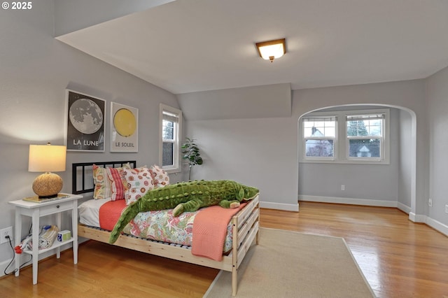 bedroom featuring arched walkways, vaulted ceiling, baseboards, and wood finished floors