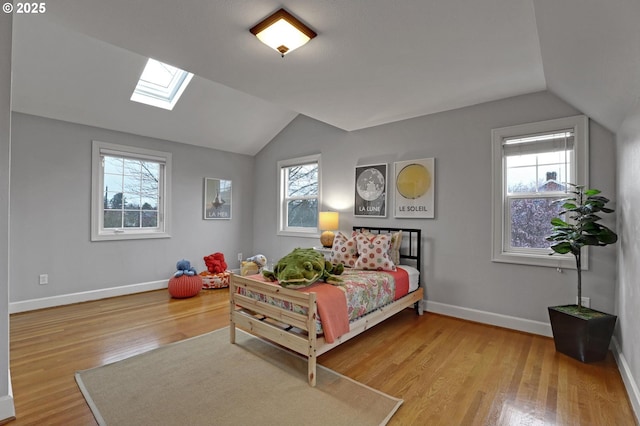 bedroom featuring lofted ceiling with skylight, multiple windows, wood finished floors, and baseboards