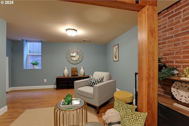 sitting room with visible vents, brick wall, baseboards, and wood finished floors