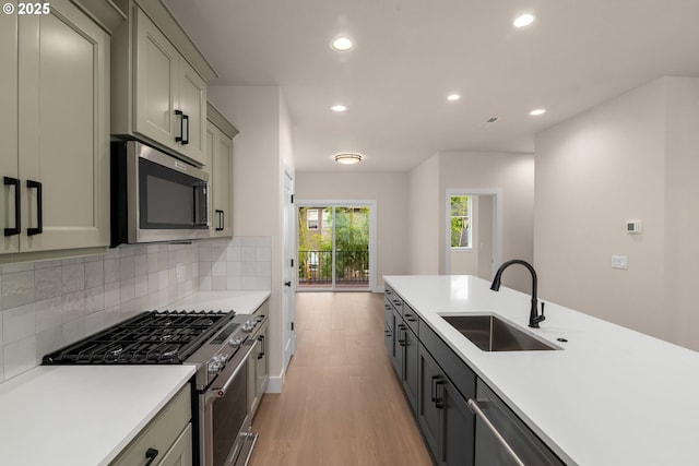 kitchen featuring backsplash, sink, light hardwood / wood-style flooring, gray cabinetry, and stainless steel appliances