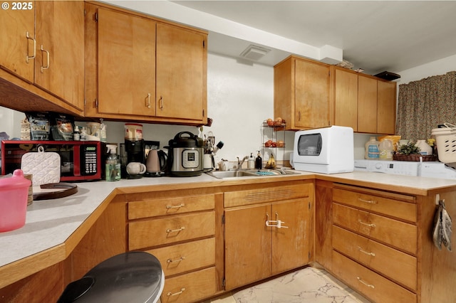 kitchen with brown cabinetry, white microwave, marble finish floor, light countertops, and a sink