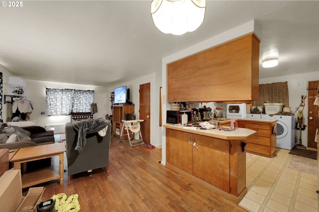 kitchen with light wood finished floors, washer / clothes dryer, brown cabinets, a peninsula, and light countertops