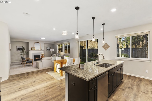 kitchen featuring sink, light stone counters, light hardwood / wood-style flooring, dishwasher, and a kitchen island with sink