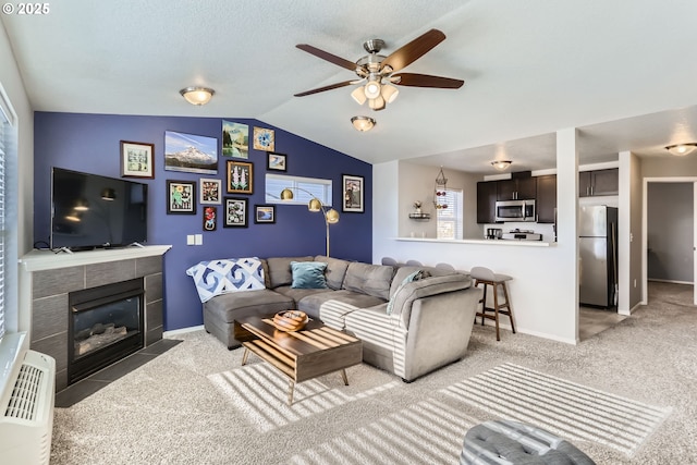 living room featuring a tiled fireplace, lofted ceiling, light colored carpet, and ceiling fan