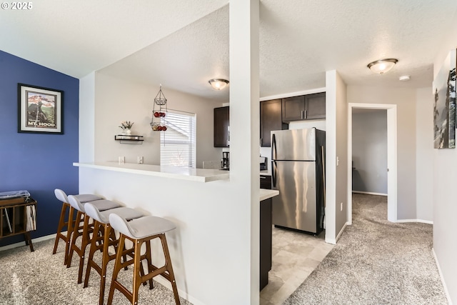 kitchen featuring a breakfast bar, dark brown cabinets, a textured ceiling, stainless steel refrigerator, and kitchen peninsula