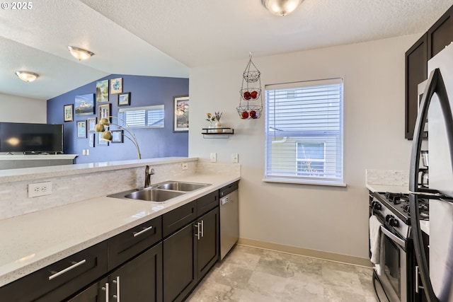 kitchen with sink, dark brown cabinets, stainless steel appliances, a textured ceiling, and vaulted ceiling