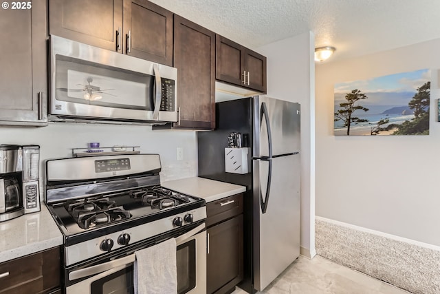 kitchen featuring appliances with stainless steel finishes, ceiling fan, light stone counters, dark brown cabinetry, and a textured ceiling