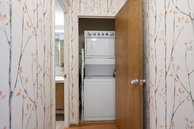 clothes washing area featuring stacked washer / dryer, wallpapered walls, and laundry area