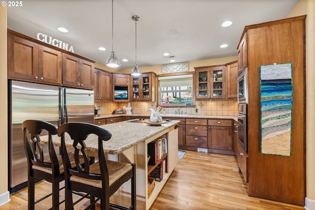 2809 Dead Indian Memorial Rd, Ashland, OR 97520 - kitchen featuring decorative backsplash, a kitchen island, brown cabinets, built in appliances, and light wood-style flooring