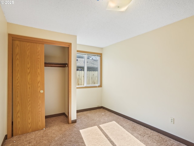 unfurnished bedroom with a textured ceiling, carpet, a closet, and baseboards