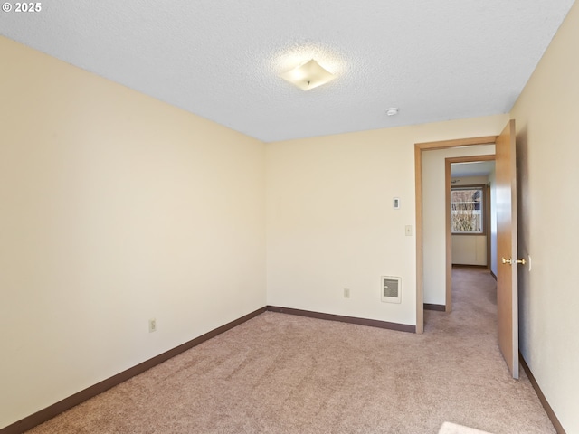 empty room featuring visible vents, light colored carpet, a textured ceiling, and baseboards