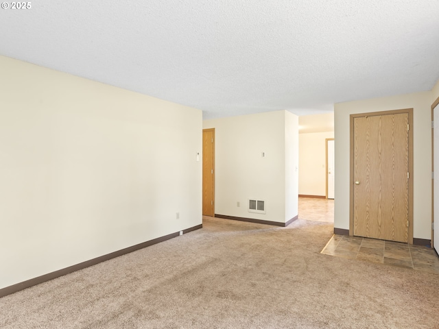 carpeted empty room with baseboards, visible vents, and a textured ceiling