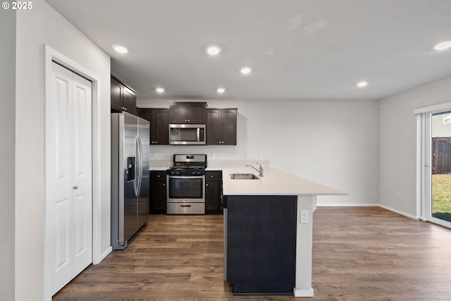 kitchen with sink, appliances with stainless steel finishes, dark brown cabinetry, dark hardwood / wood-style flooring, and kitchen peninsula