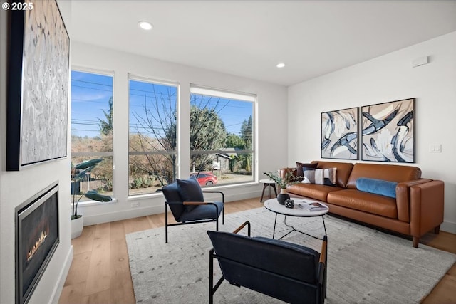 living area with light wood-style floors, a warm lit fireplace, recessed lighting, and baseboards