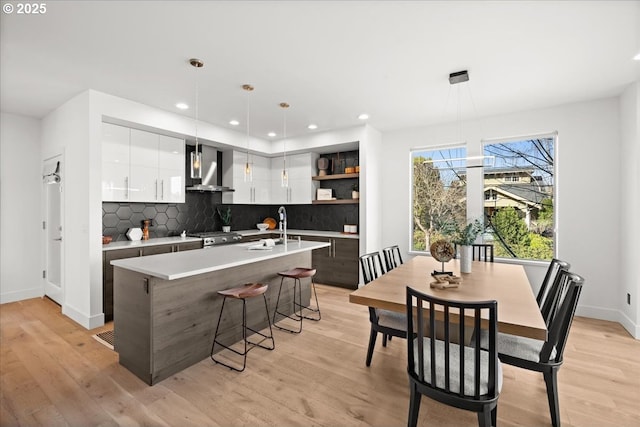 kitchen with wall chimney range hood, open shelves, modern cabinets, white cabinetry, and light countertops