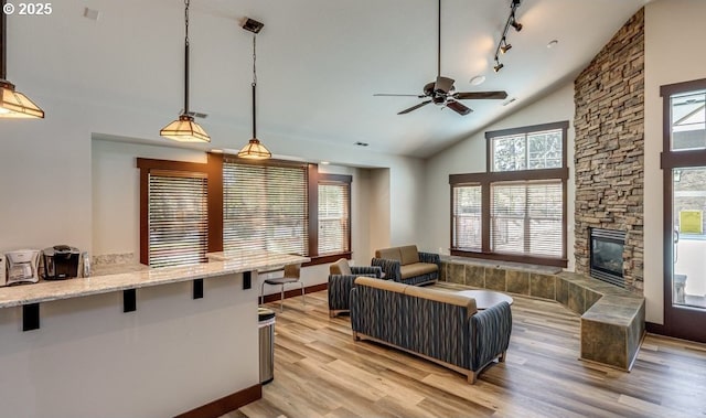 living room with track lighting, a stone fireplace, vaulted ceiling, ceiling fan, and light hardwood / wood-style flooring