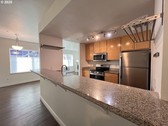 kitchen with kitchen peninsula, dark wood-type flooring, appliances with stainless steel finishes, light brown cabinetry, and dark stone counters