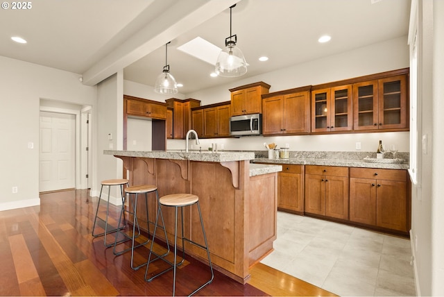 kitchen with a kitchen bar, light stone counters, pendant lighting, and a center island with sink