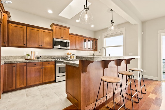 kitchen with beam ceiling, hanging light fixtures, a kitchen island with sink, appliances with stainless steel finishes, and a kitchen breakfast bar