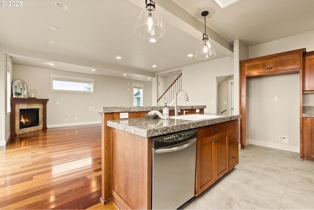 kitchen featuring decorative light fixtures, light hardwood / wood-style floors, a center island with sink, sink, and light stone counters