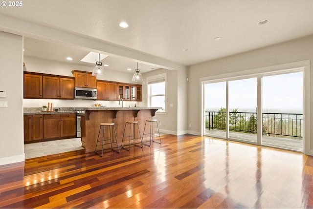 kitchen with a kitchen island, light hardwood / wood-style flooring, light stone countertops, appliances with stainless steel finishes, and a breakfast bar area