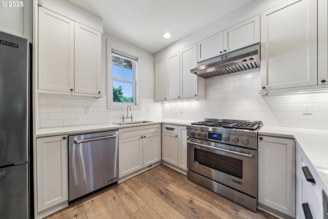 kitchen with stainless steel appliances, under cabinet range hood, a sink, light wood-style floors, and light countertops
