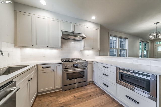 kitchen with appliances with stainless steel finishes, under cabinet range hood, recessed lighting, a chandelier, and light wood finished floors