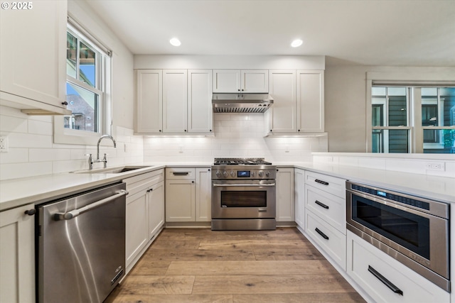 kitchen with stainless steel appliances, a sink, under cabinet range hood, light wood-type flooring, and light countertops