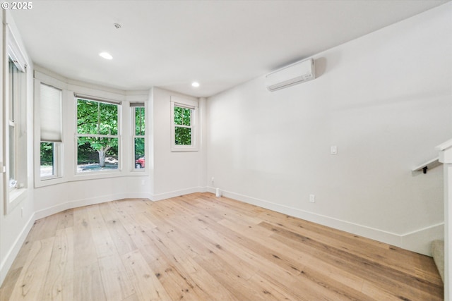 spare room featuring a wall mounted AC, light wood-style floors, baseboards, and recessed lighting