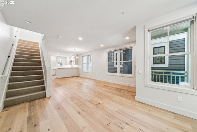 unfurnished living room with stairway, baseboards, light wood-style floors, recessed lighting, and a chandelier