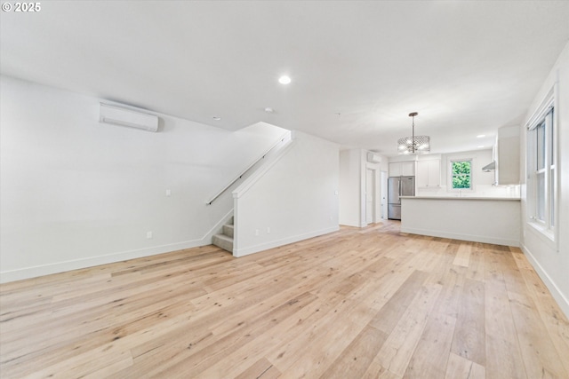 unfurnished living room featuring a chandelier, light wood-type flooring, stairs, a wall unit AC, and baseboards