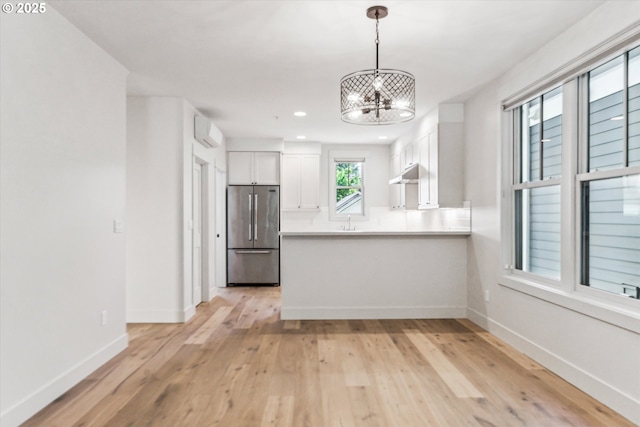 kitchen featuring freestanding refrigerator, white cabinets, a chandelier, a peninsula, and light wood finished floors