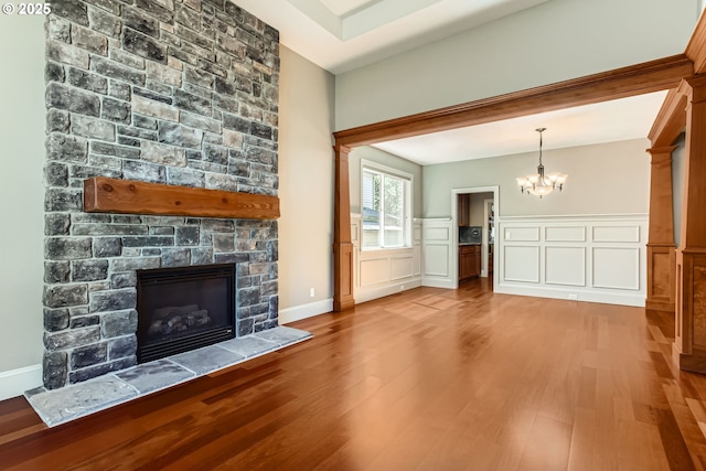 14702 SE Badger Creek Rd, Happy Valley, OR 97086 - unfurnished living room featuring a stone fireplace, wood finished floors, a chandelier, wainscoting, and a decorative wall