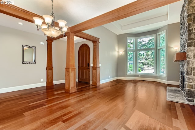 14702 SE Badger Creek Rd, Happy Valley, OR 97086 - unfurnished living room featuring ornate columns, wood finished floors, a chandelier, a tray ceiling, and a stone fireplace