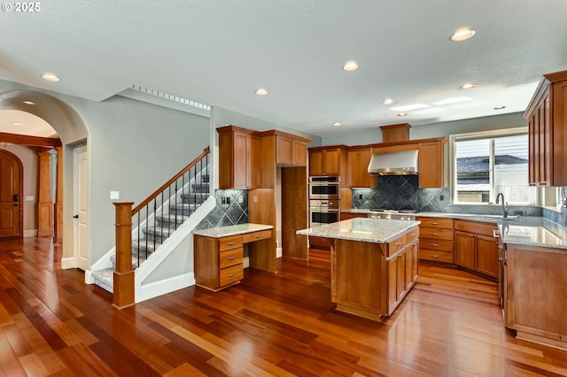 14702 SE Badger Creek Rd, Happy Valley, OR 97086 - kitchen with wall chimney exhaust hood, brown cabinets, dark wood-type flooring, and recessed lighting