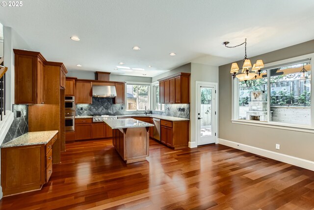14702 SE Badger Creek Rd, Happy Valley, OR 97086 - kitchen featuring brown cabinetry, wall chimney exhaust hood, stainless steel appliances, dark wood-style flooring, and recessed lighting