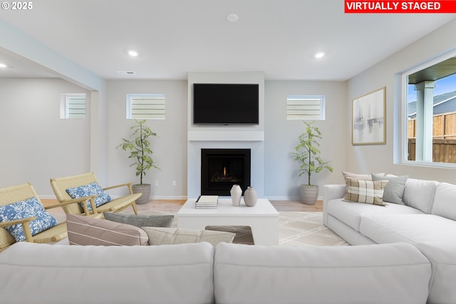 living area featuring a warm lit fireplace, recessed lighting, visible vents, light wood-style floors, and baseboards