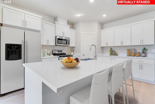 kitchen with light countertops, appliances with stainless steel finishes, a sink, and a center island with sink