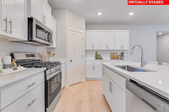 kitchen featuring appliances with stainless steel finishes, white cabinets, light countertops, and a sink