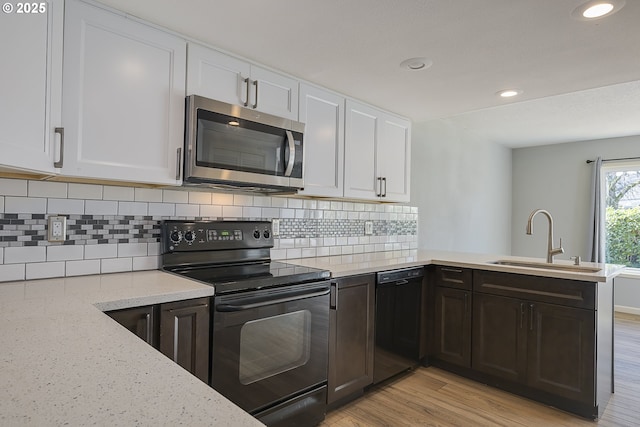 kitchen featuring a sink, a peninsula, white cabinetry, black appliances, and light wood finished floors