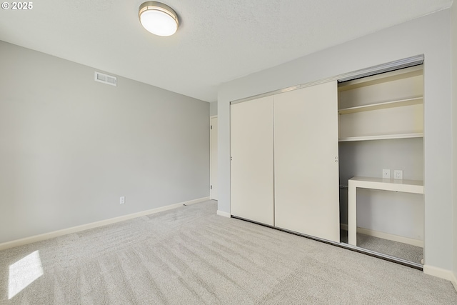 unfurnished bedroom featuring a closet, baseboards, a textured ceiling, carpet floors, and visible vents